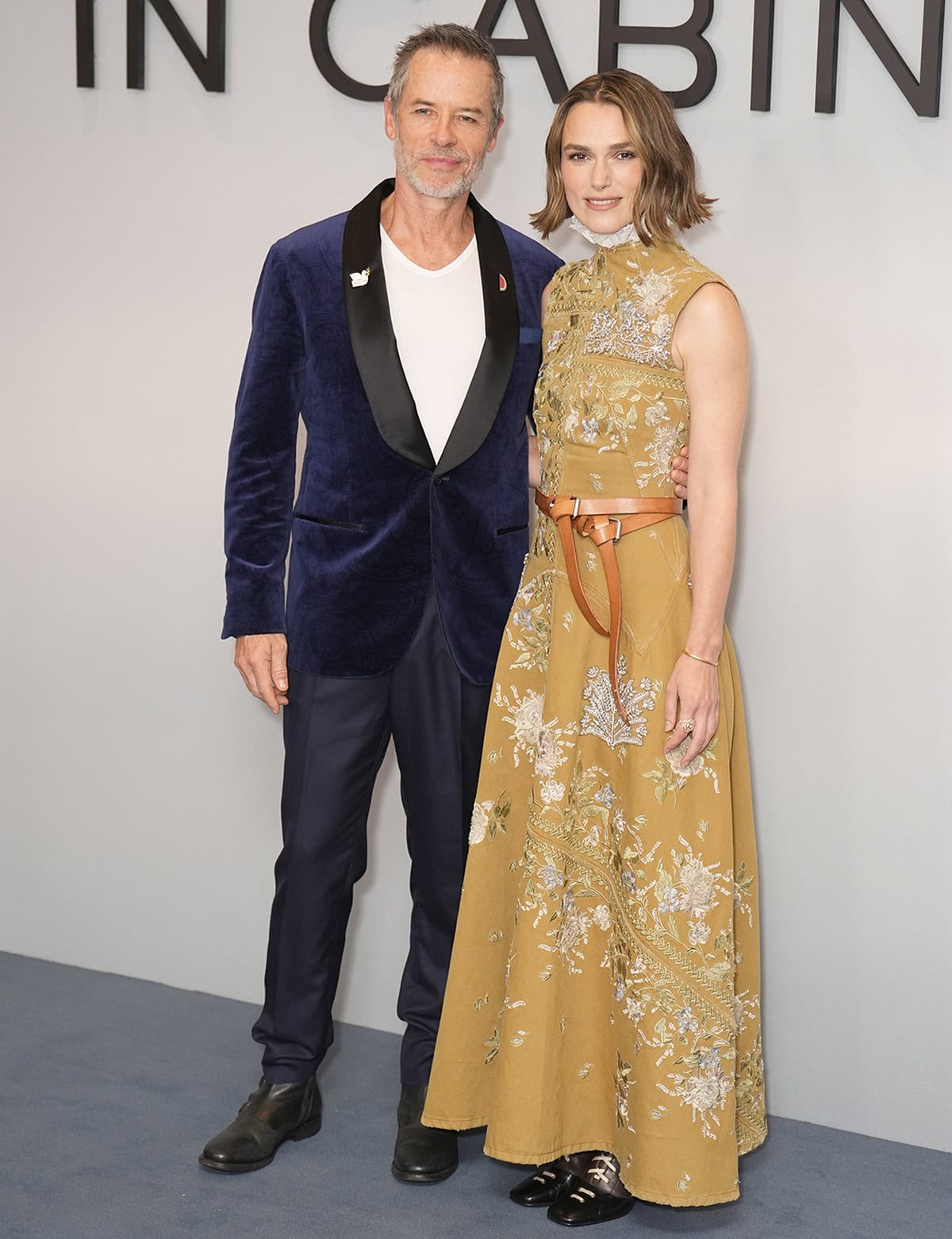 Guy Pearce and Keira Knightley at the London premiere of The Woman in Cabin 10 at BAFTA Piccadilly on September 25, 2025 — Pearce in a velvet tuxedo jacket and Knightley in a mustard-yellow embroidered Erdem gown cinched with a leather belt, styled with equestrian-inspired boots