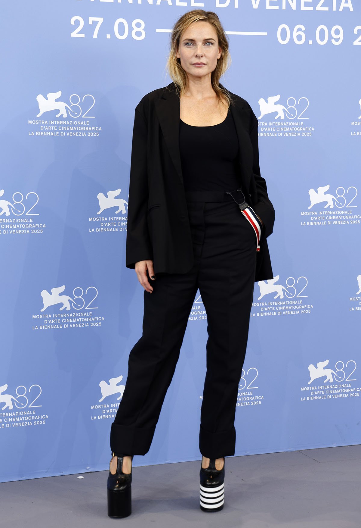 Rebecca Ferguson opts for her signature androgynous style, wearing a black Thom Browne suit with a black scoop-neck bodysuit and the label's signature striped suspenders at the Venice photocall for A House of Dynamite