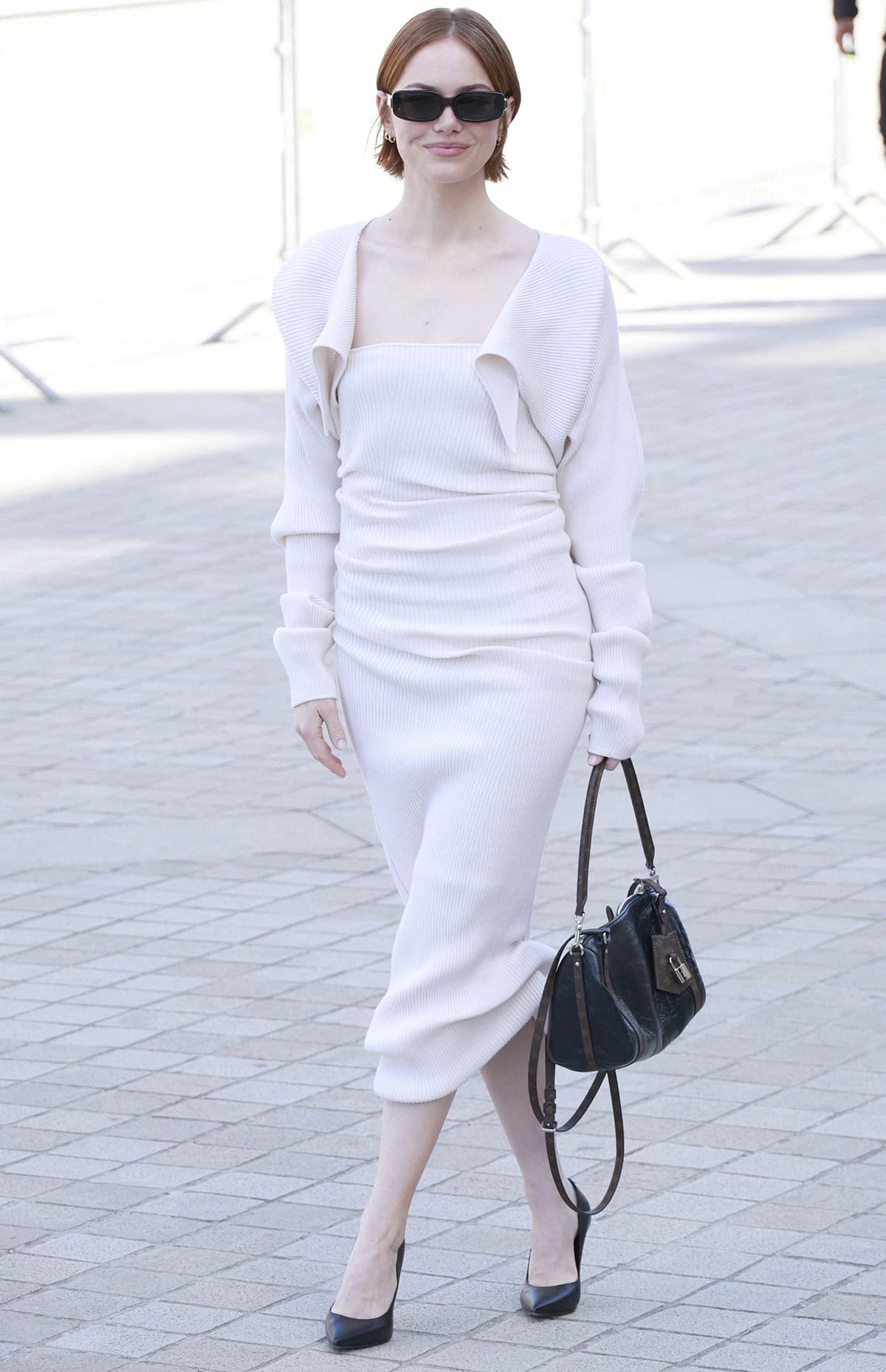 Emma Stone embraces minimalist elegance in a rib-knit white Louis Vuitton midi dress and cardigan set, paired with black pumps for timeless contrast