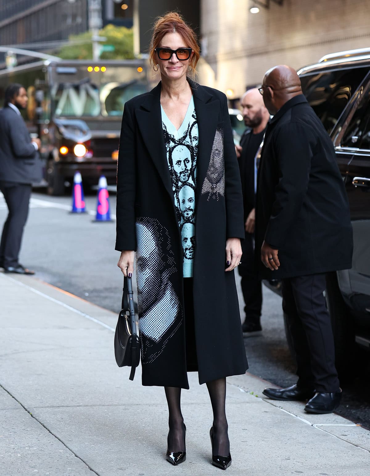 Julia Roberts honors Shakespeare and After the Hunt director Luca Guadagnino in a black Libertine coat embellished with studded halftone portraits and a white Twinship “The Luca” sweater dress, styled with sheer black tights, a Polène “Numéro Dix” bag, and Jimmy Choo “Ixia” pumps on October 1, 2025, in New York City