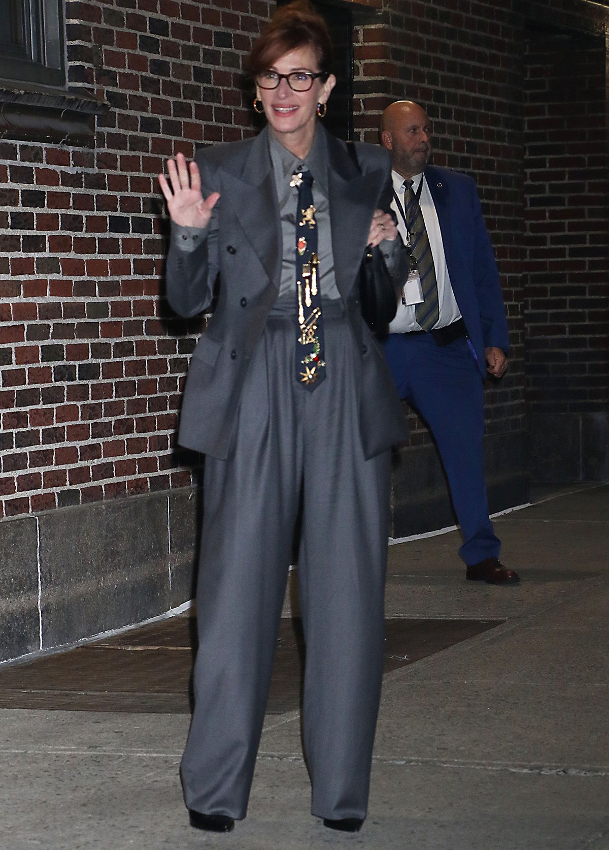 Julia Roberts channels timeless menswear elegance in a gray Salon 1884 suit with a peaked-lapel blazer, pleated wide-leg trousers, and a vintage brooch-adorned tie for her appearance on The Late Show with Stephen Colbert on October 1, 2025, in New York City