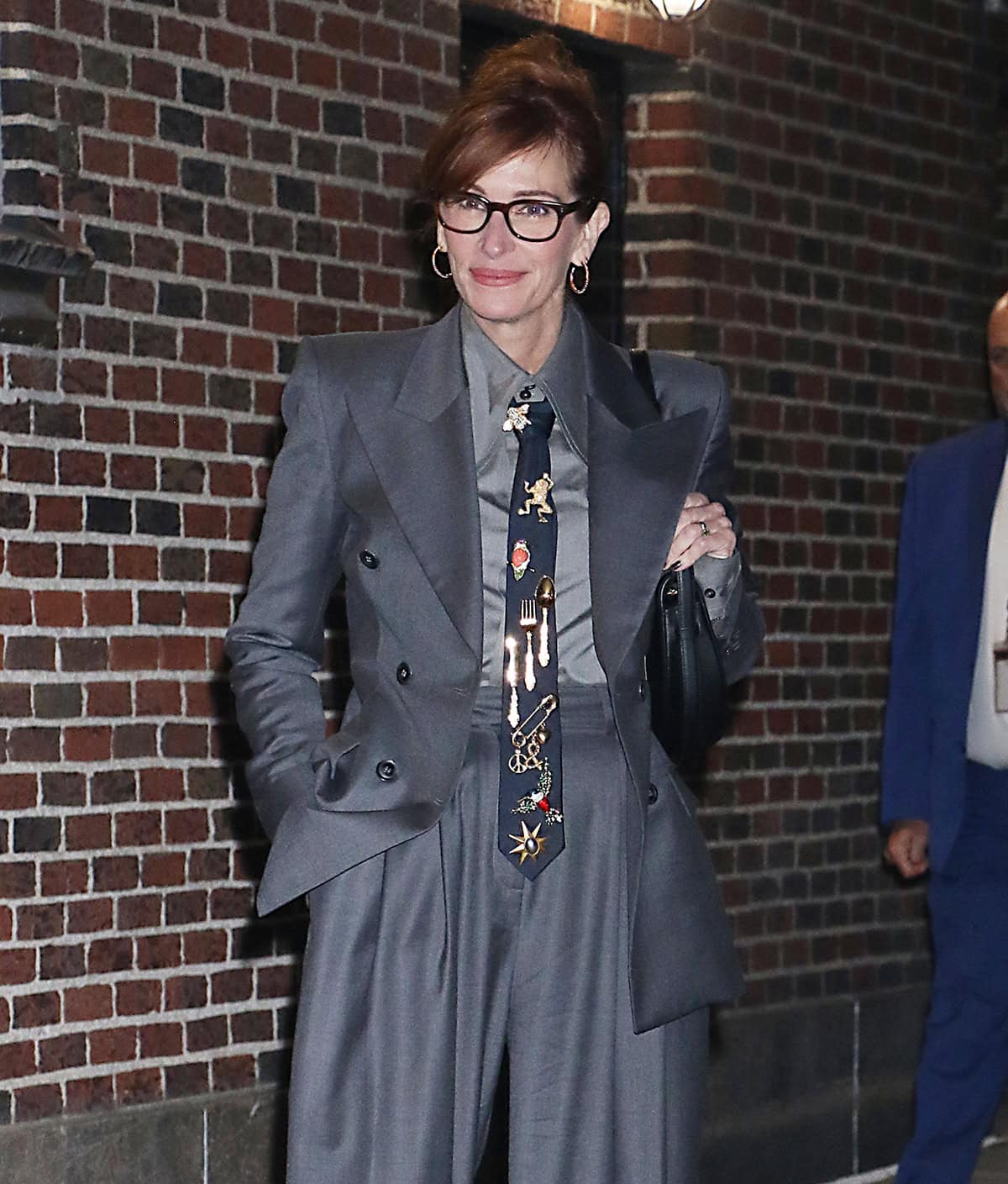 Julia Roberts channels her inner professor, styling her tailored business wear with eyeglasses and a navy necktie adorned with whimsical brooches