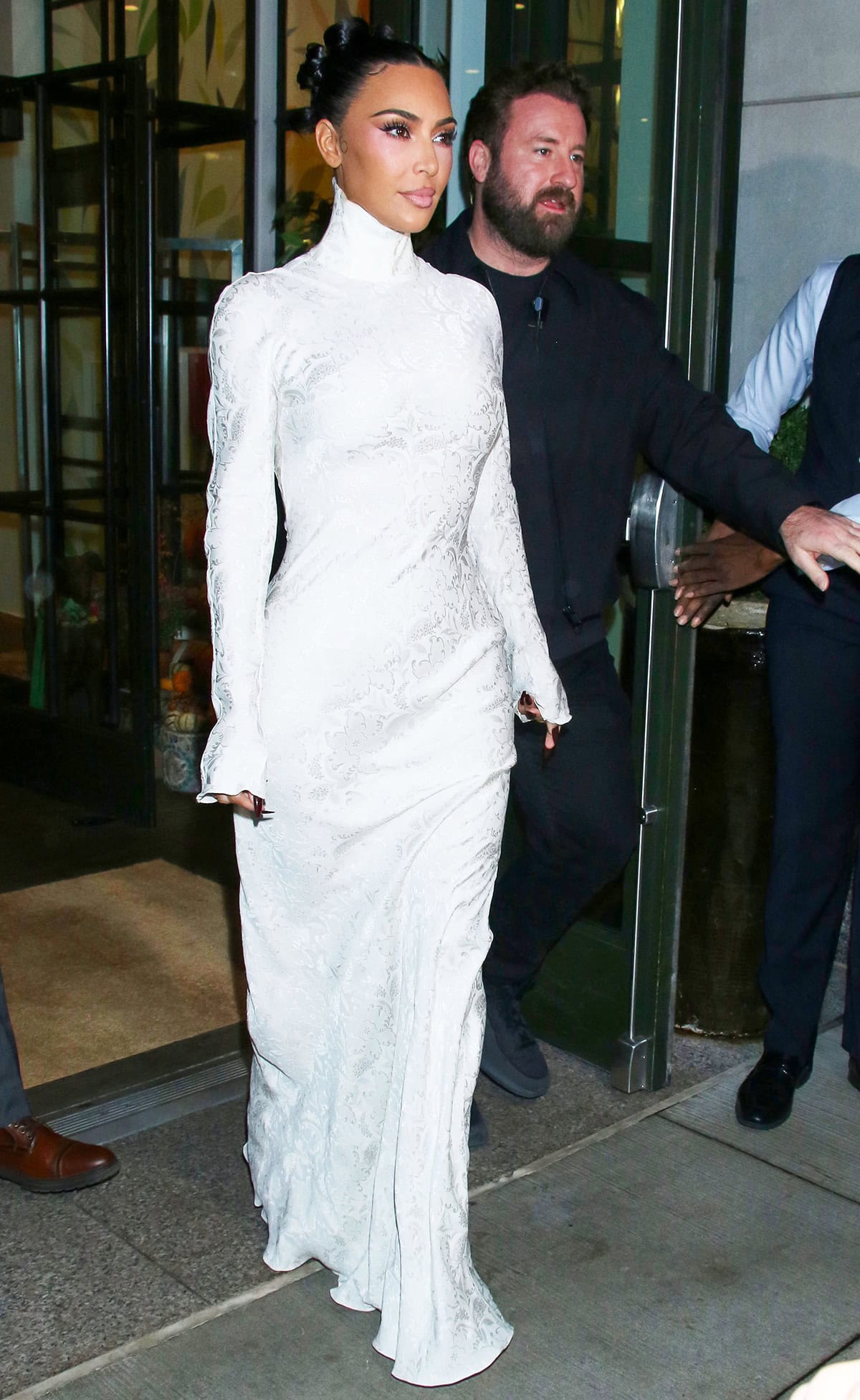 Kim Kardashian opts for a minimalist bridal-style dress from John Galliano's archives, made of white jacquard fabric with a high neck, flared sleeves, and a sweeping skirt