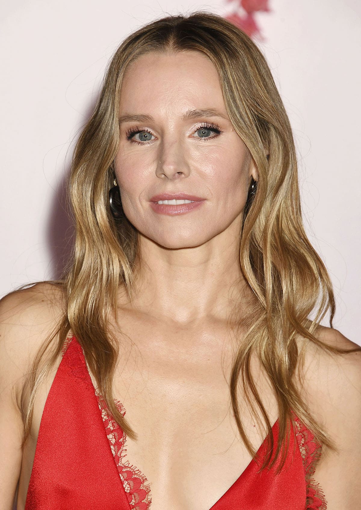 Kristen Bell wears her blonde hair in loose waves and highlights her blue eyes with mascara, paired with rosy blush and soft pink lipstick