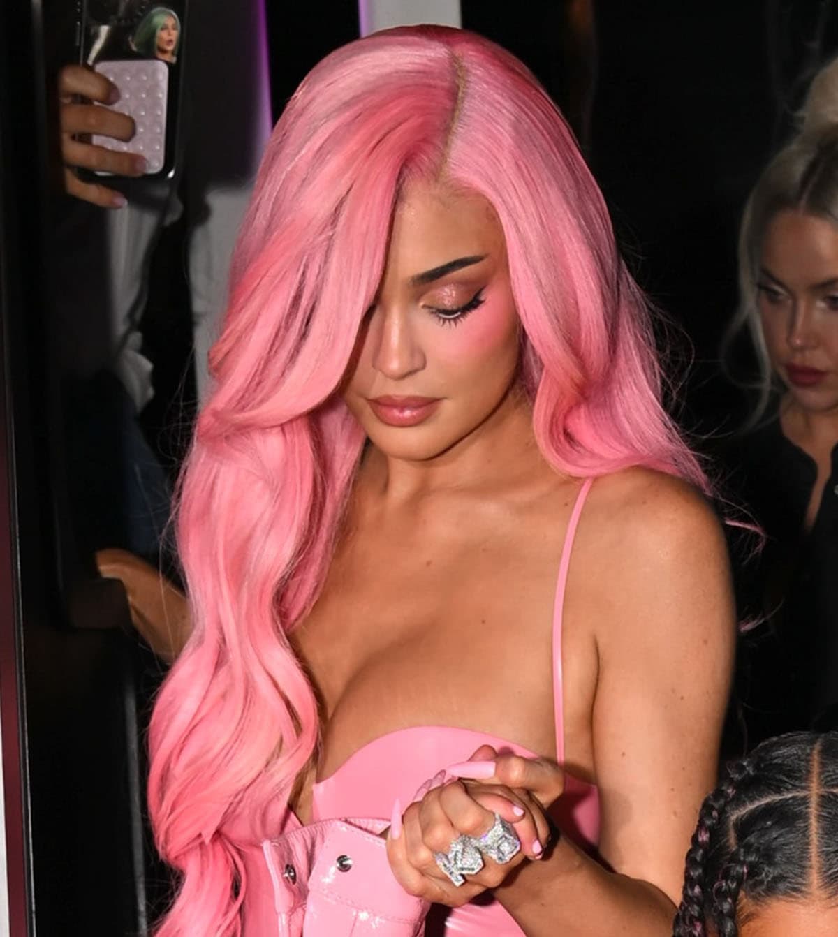 Kylie Jenner highlights her features with pink makeup using Kylie Cosmetics, wears a long, wavy pink wig from Kendra’s Boutique, and accessorizes with statement diamond rings, including the Ailes Jewelry Full Diamond Chaines Ring