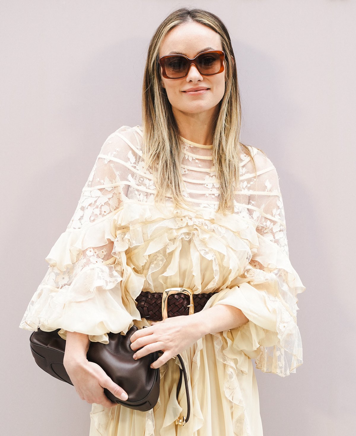 Olivia Wilde enhances her boho ensemble with a brown leather Zimmerman “Halcyon” clutch, a brown braided belt, and tortoiseshell square sunglasses