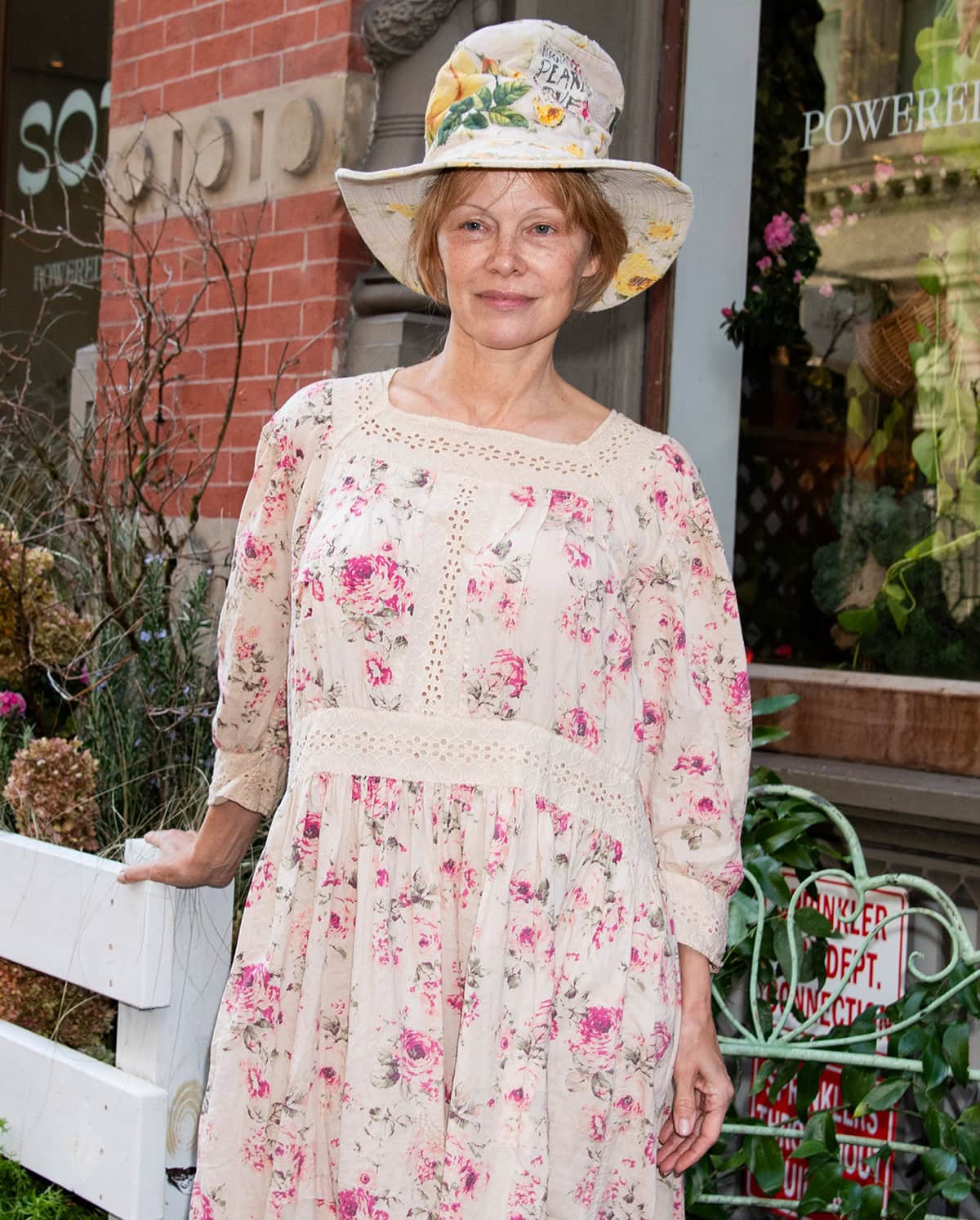Pamela Anderson goes maximalist, pairing her Magnolia Pearl floral dress with a floral top hat and green ladybug socks