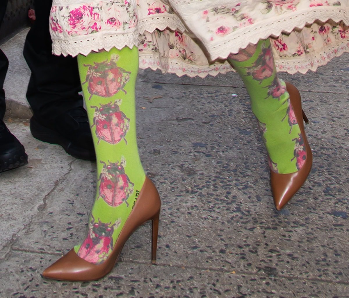 Pamela Anderson adds an unexpected twist to her floral Magnolia Pearl dress, pairing whimsical green ladybug-print socks with polished brown pointed-toe pumps — a bold contrast that blends cottagecore romance with offbeat charm