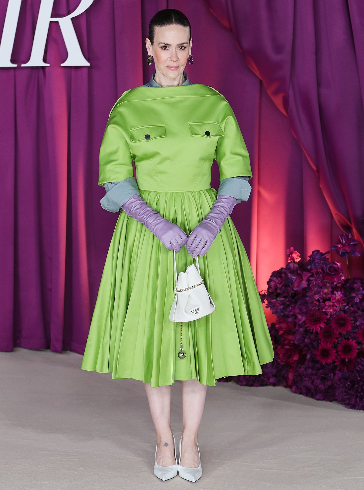 Sarah Paulson steals the spotlight in a lime-green A-line midi dress by Prada, featuring a boxy bodice with chest pockets, epaulets, and a feminine pleated skirt