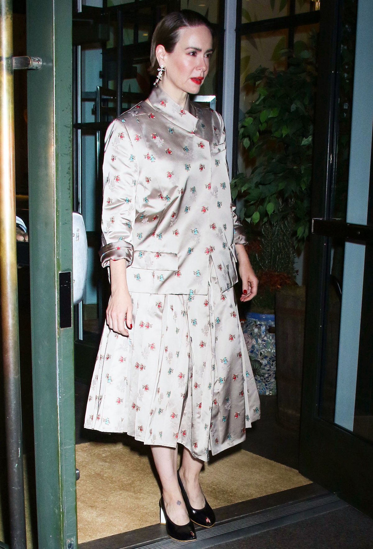 Sarah Paulson embraces retro glamour in a beige satin Tory Burch outfit featuring a shirt and a matching pleated A-line midi skirt adorned with tonal floral prints with pops of red and blue