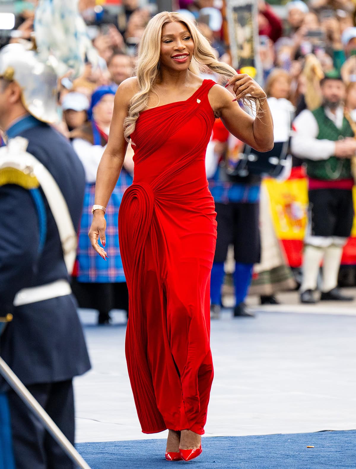 Serena Williams radiates power and elegance in a sculptural red Gaurav Gupta gown with a one-shoulder neckline, architectural pleating, and matching patent pointed-toe pumps