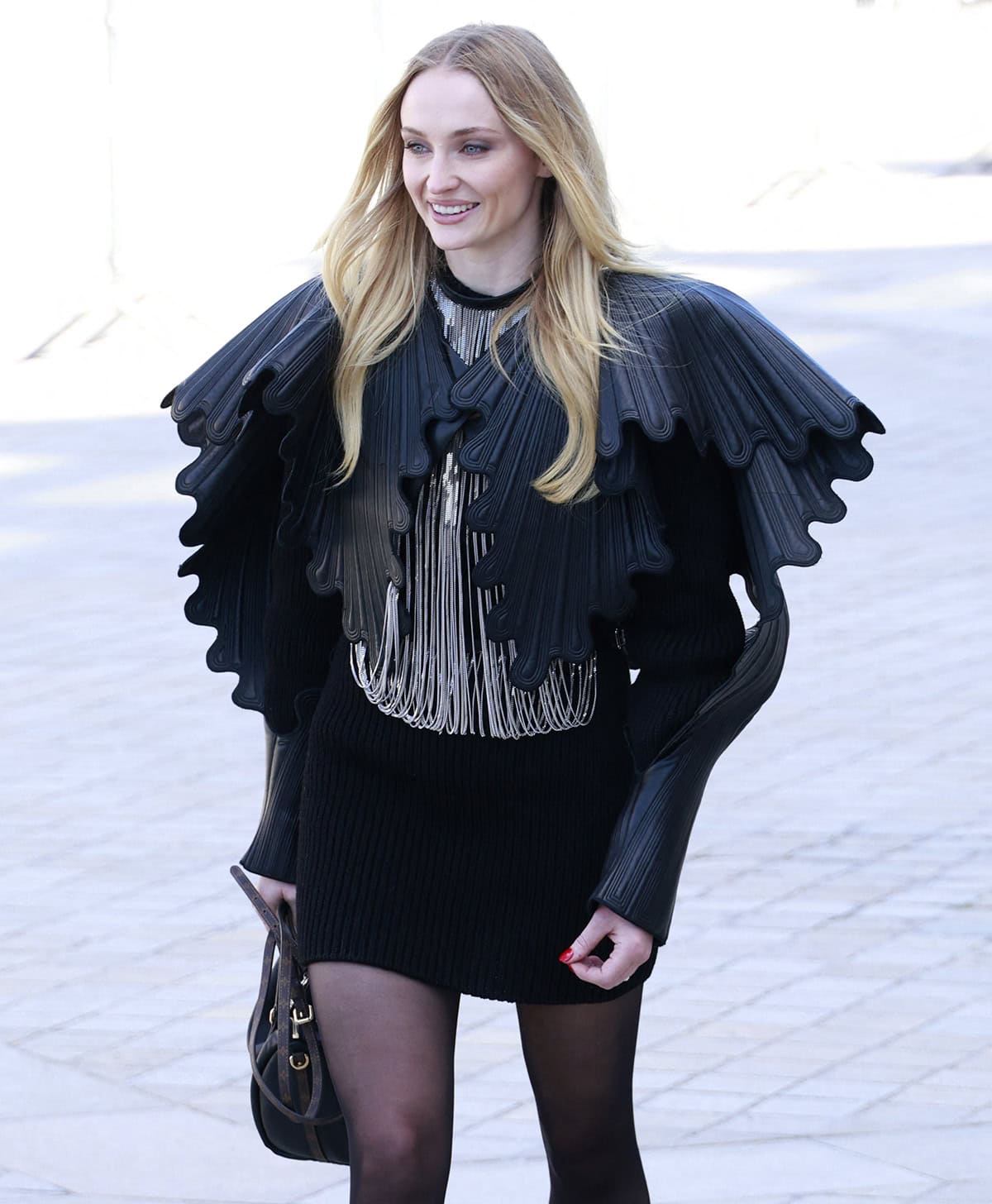 Sophie Turner commands attention in an avant-garde winged leather jacket layered over a silver-fringed top and ribbed mini skirt by Louis Vuitton