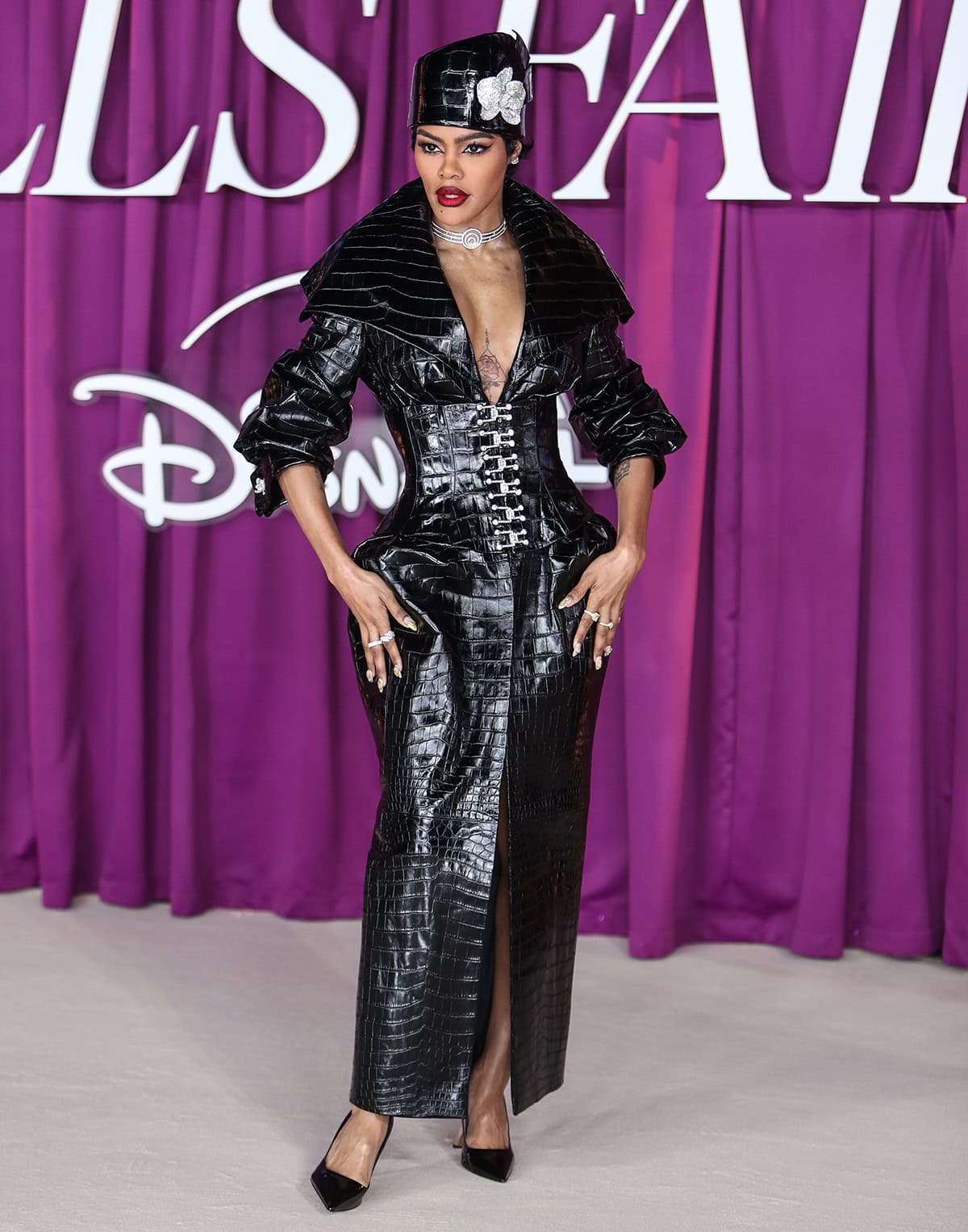 Teyana Taylor opts for a theatrical black croc-embossed leather coat dress by Tamara Ralph featuring an exaggerated collar, rolled-up sleeves, crystal fastenings, and a thigh-high center slit