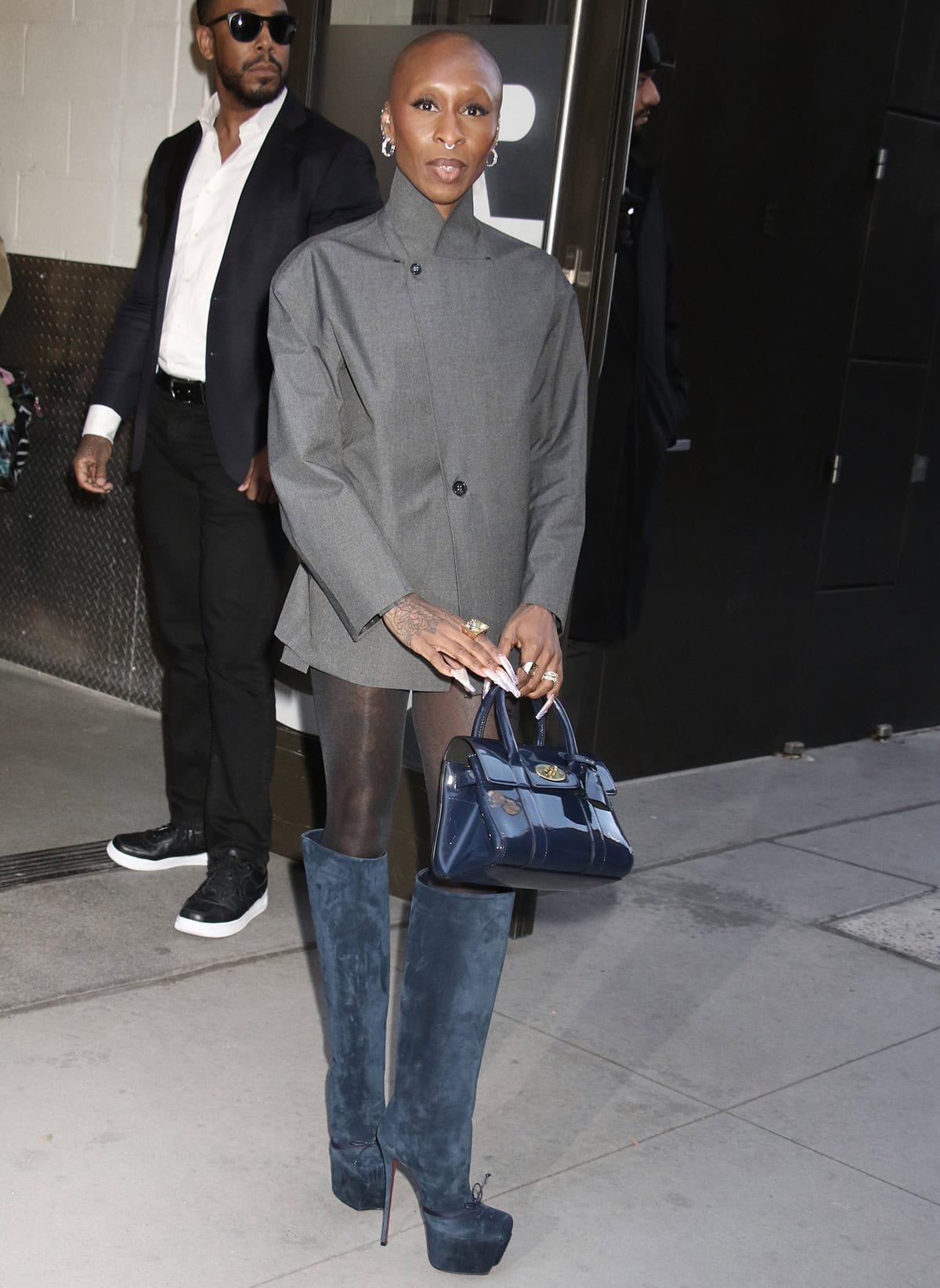 Cynthia Erivo pairs her blue-gray suede boots with a dark gray Coperni short suit composed of a lapel-free blazer with a stand-up collar and two buttons and high-waisted shorts