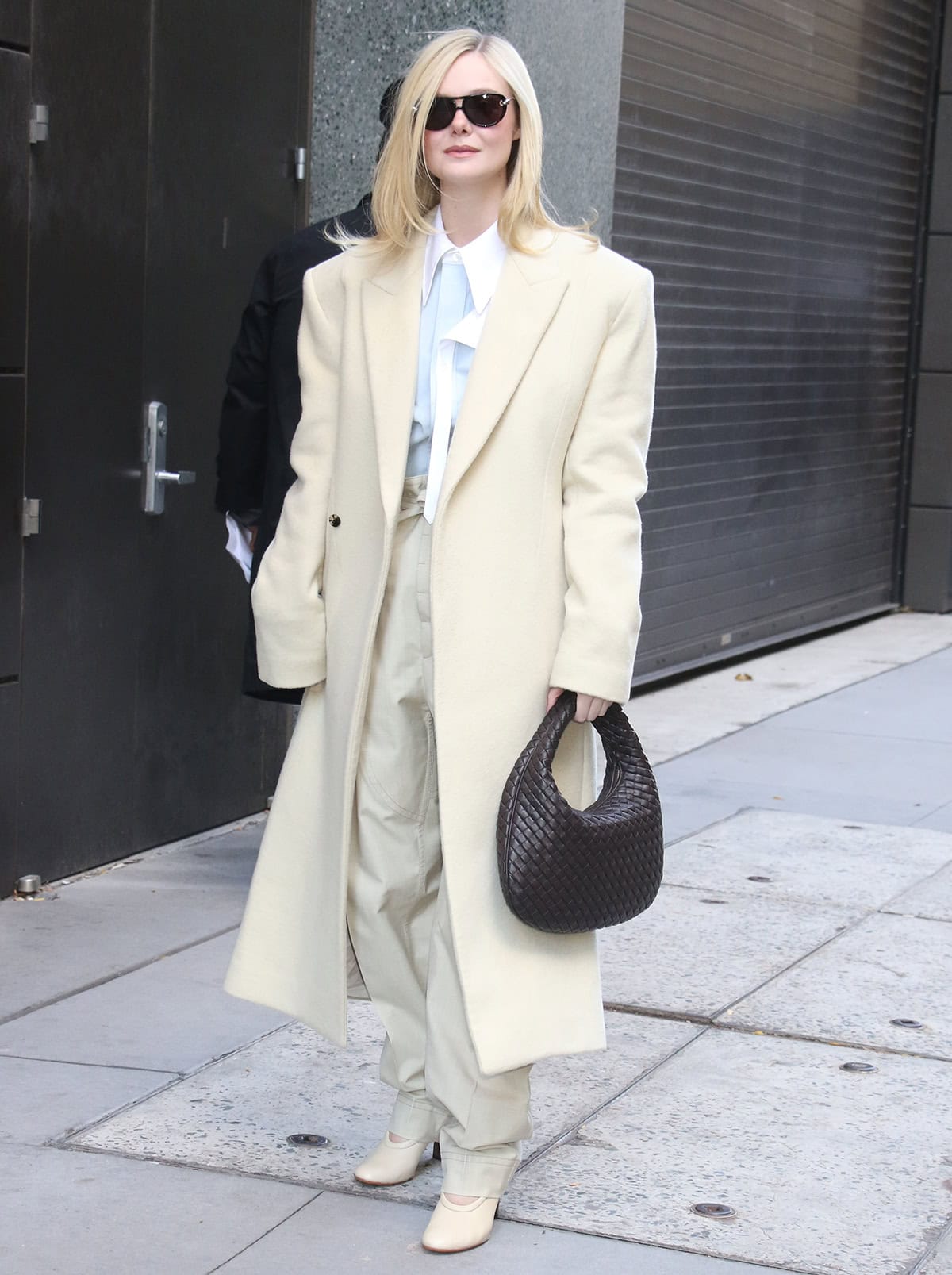 Elle Fanning embraces soft power dressing in a creamy Bottega Veneta coat, matching trousers with a tie waist, and a light blue shirt with a white collar outside the Live With Kelly & Mark studios