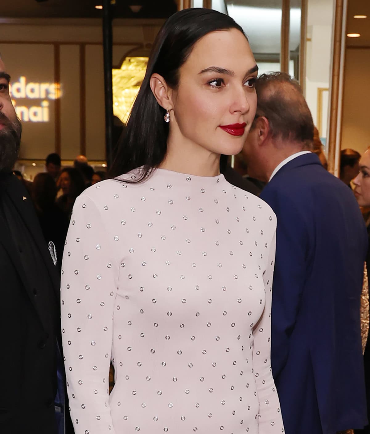 Gal Gadot adds a pop of color to her look with bold red lipstick and styles her raven hair straight and tucked behind her ears