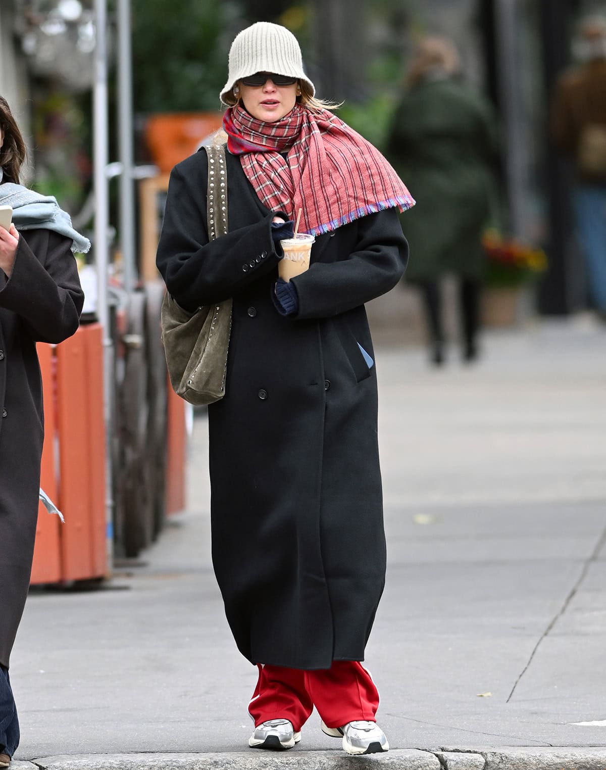 Jennifer Lawrence keeps things cozy in a black Almada Label coat, red Loewe track pants, and a Shahkaar scarf while out and about in New York City on October 28, 2025