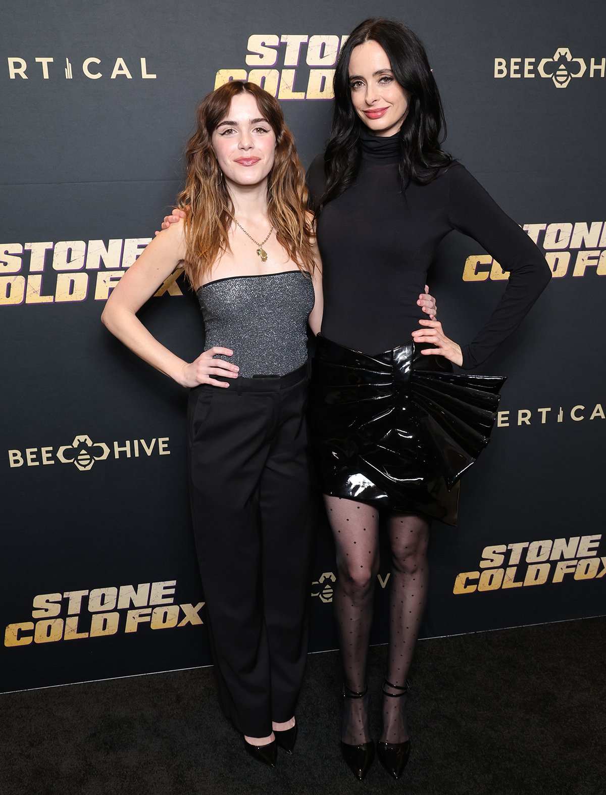 Kiernan Shipka and Krysten Ritter showcase their contrasting proportions and polished monochrome style at the Stone Cold Fox Los Angeles special screening, with 5’2” Shipka in glittery gray separates beside the statuesque 5’9¼” Ritter in a sleek Balmain mini skirt and black D’Orsay heels