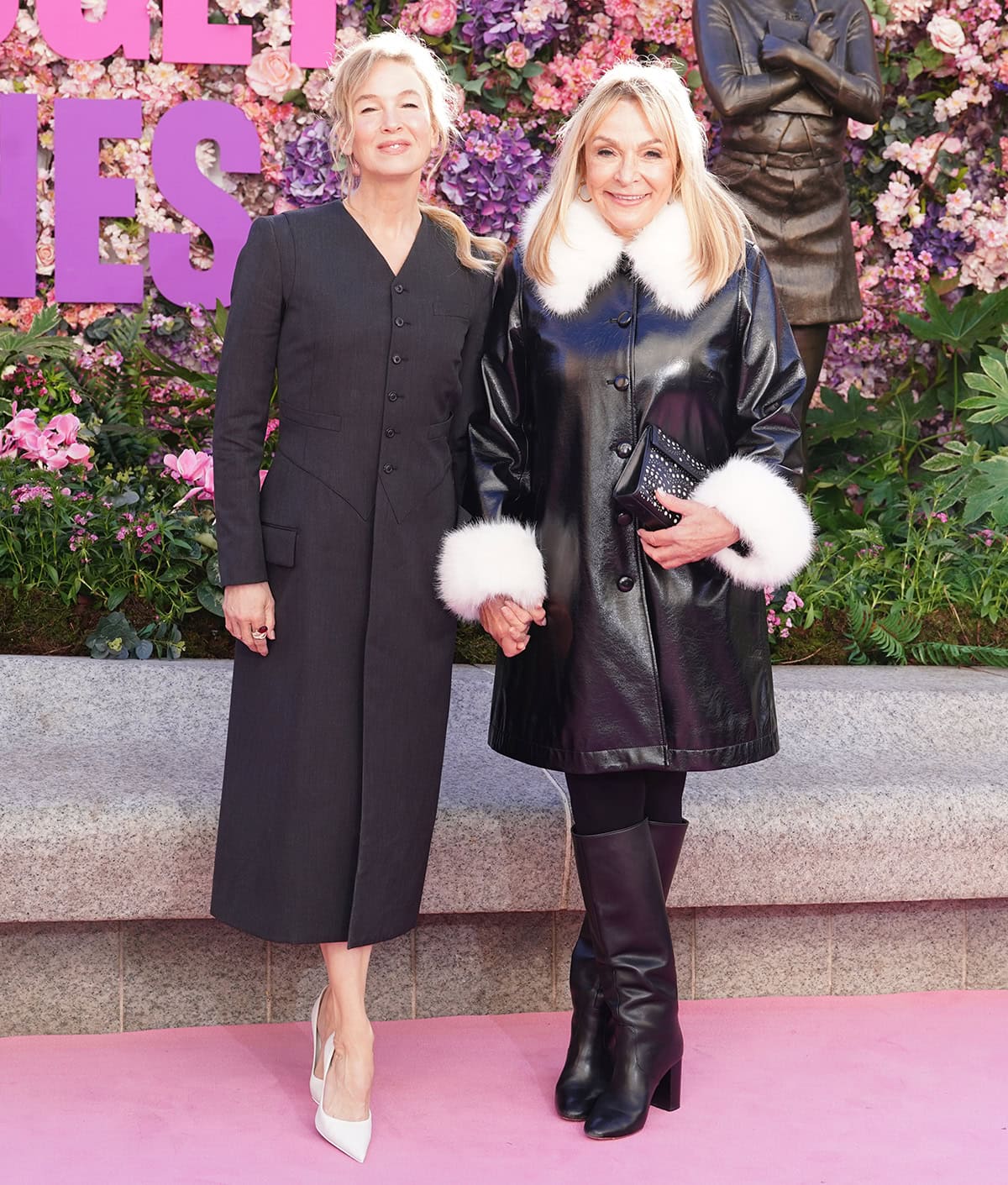 Renée Zellweger steps out in a minimalist black coat dress paired with sculptural white pointed-toe pumps, while Helen Fielding complements her in a black leather coat with white faux-fur trim and sleek heeled boots at the Bridget Jones statue unveiling in Leicester Squar