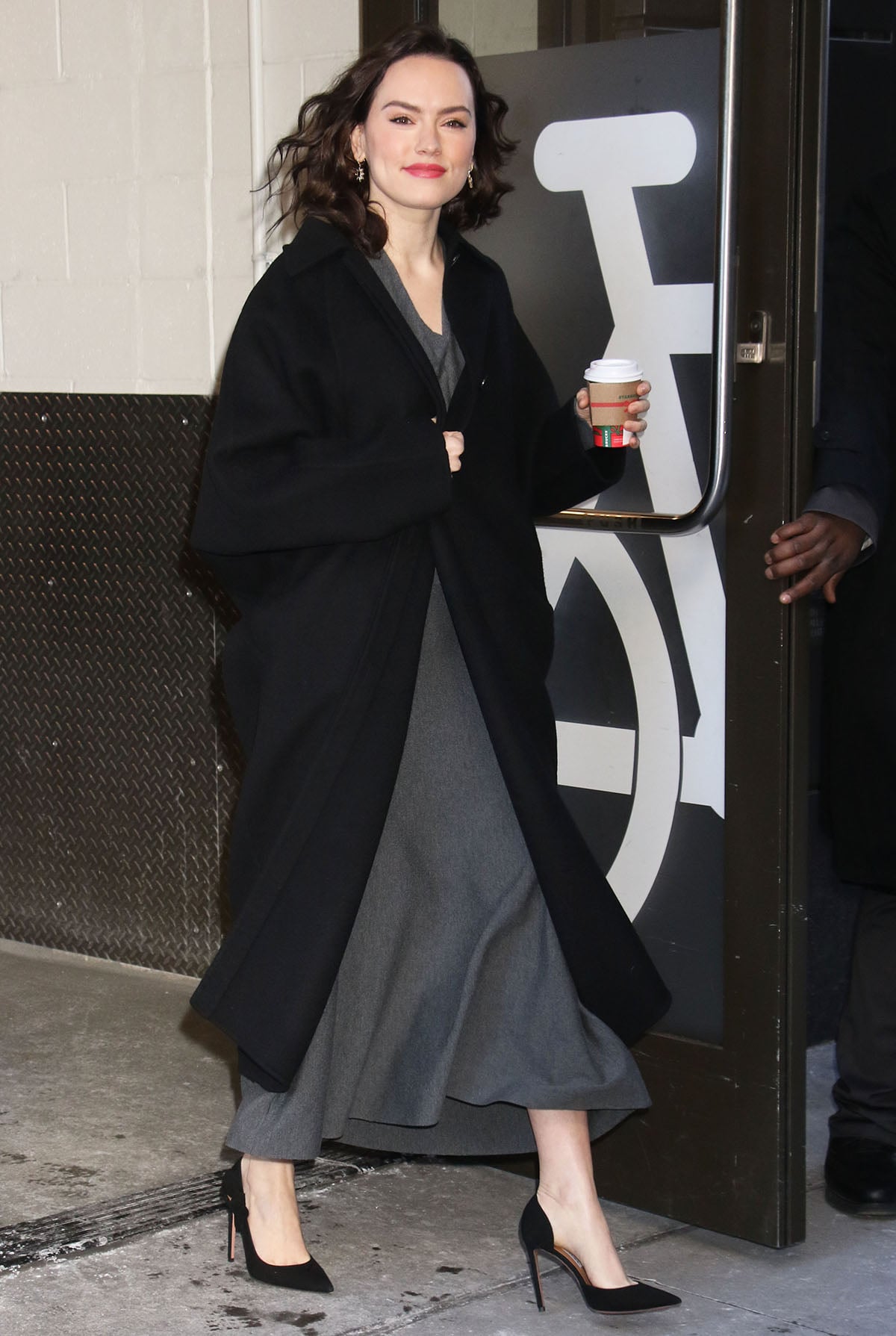 Daisy Ridley keeps a sophisticated look, pairing her black Aquazzura pumps with a gray dress and a black coat for her guest appearance on Live with Kelly and Mark
