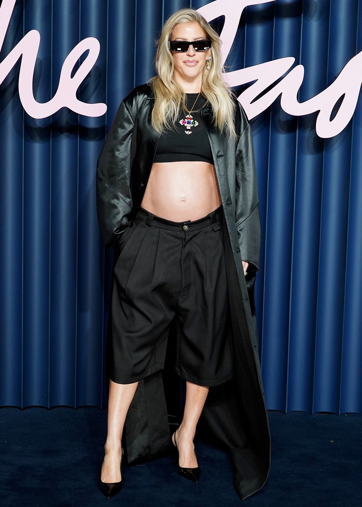 Ellie Goulding shows off her baby bump in a ribbed crop top and bermuda shorts by Willy Chavarria with a Matrix-style satin coat