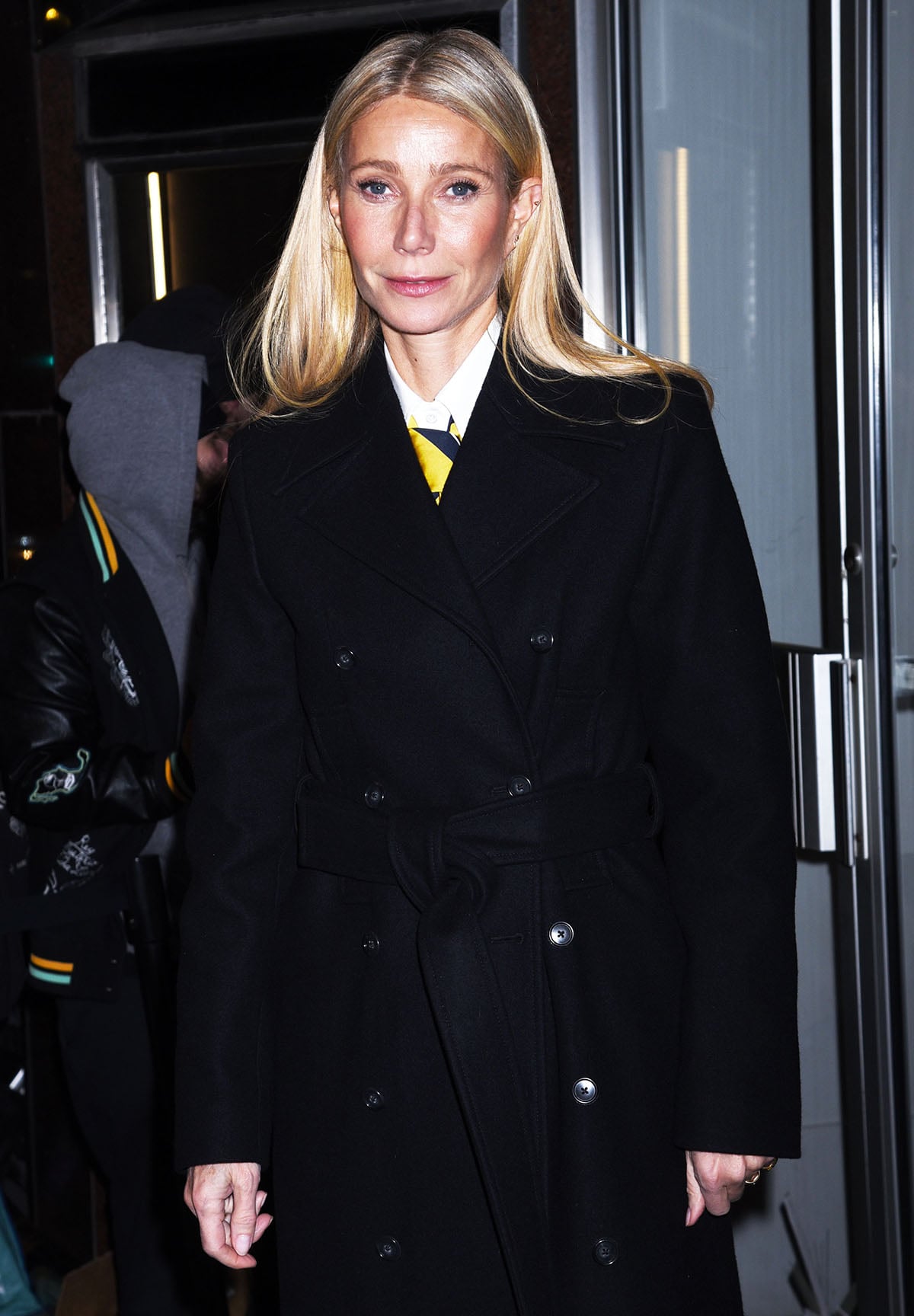 Gwyneth Paltrow opts for a polished, understated look, wearing a double-breasted black coat with a white shirt and a yellow-and-navy striped necktie for the Marty Supreme film talk at the DGA Theatre