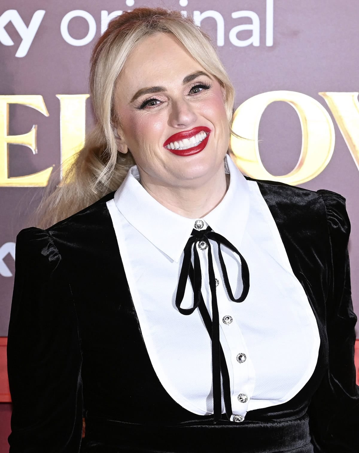 Rebel Wilson adds a pop of color to her vintage-style black-and-white ensemble with bright red lipstick and rosy blush