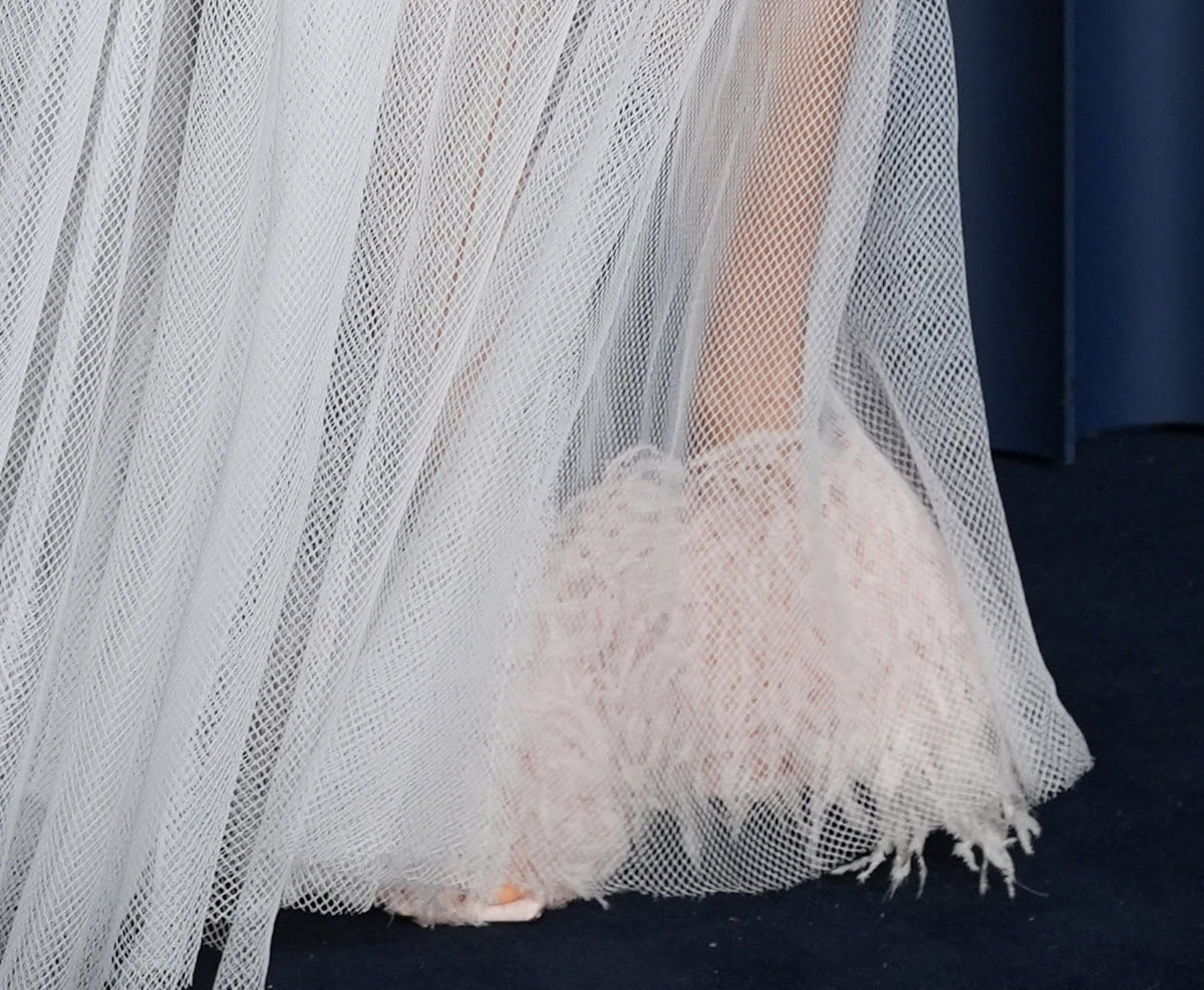 Sienna Miller’s sheer diamond-net gown reveals her blush pink fuzzy Givenchy mules peeking out from beneath the hem