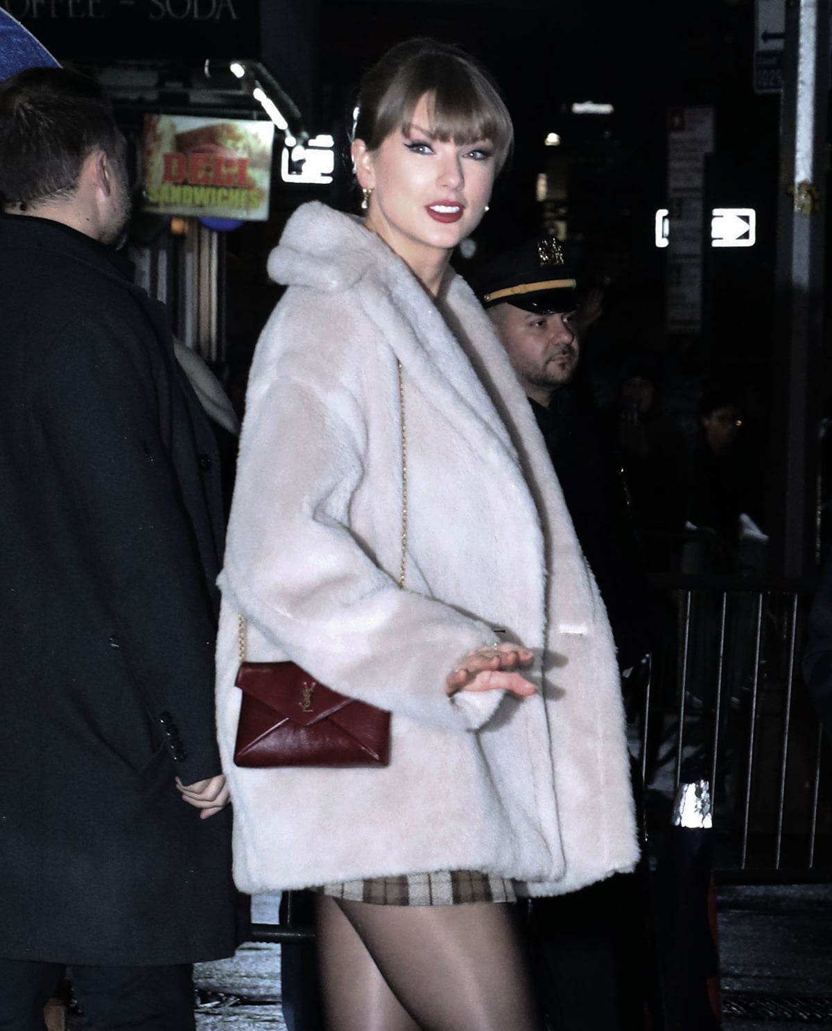 Taylor Swift styles her chic, relatable winter ensemble with Etiq Design diamond drop earrings, a burgundy Saint Laurent envelop bag, and her signature makeup