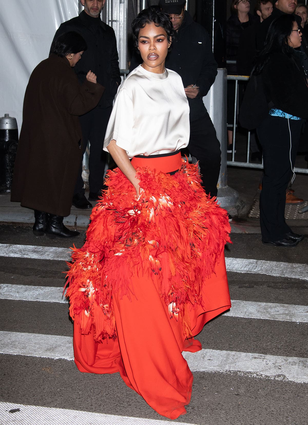 Teyana Taylor embraces festive glam in a cream satin boxy shirt and a red feather skirt from Chanel's Spring 2026 collection at the 35th Annual Gotham Film Awards