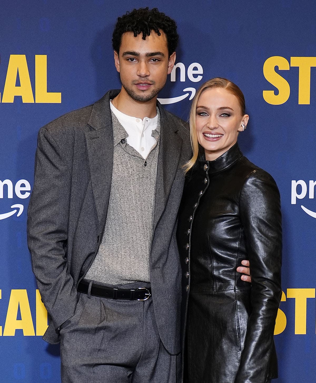 Sophie Turner, with her co-star Archie Madekwe, enhances her sleek look with a slicked-back chignon, smoky eye-makeup, and Ananya ear cuffs