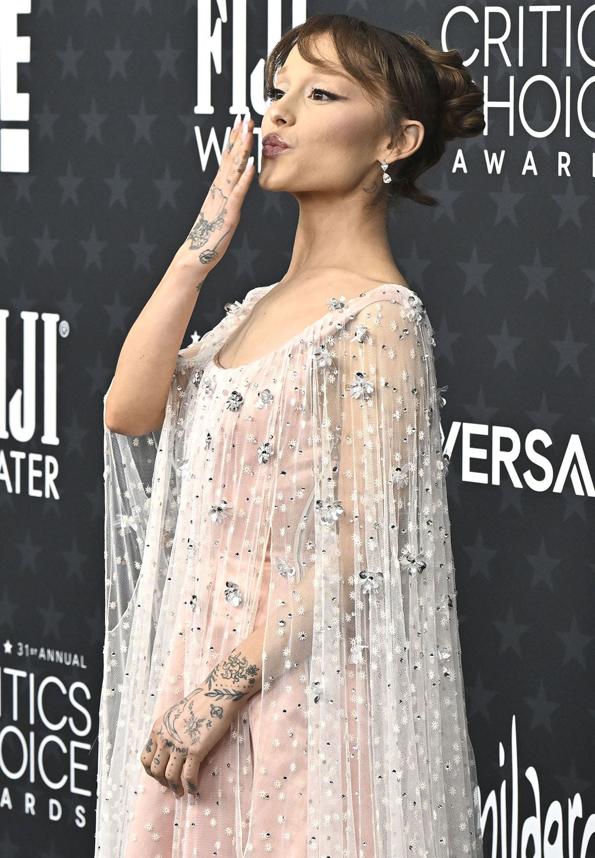 Ariana Grande styles her hair up in a loose bun with a fringe, showing off her diamond drop earrings