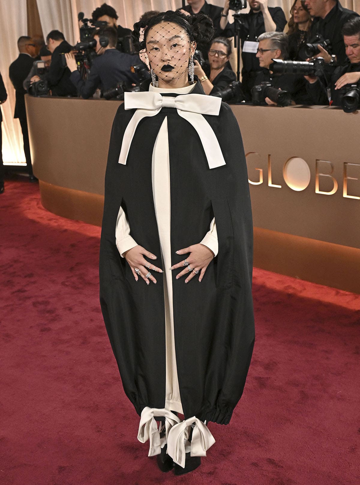 Audrey Nuna looks theatrical in a Thom Browne ensemble, featuring a black silk moiré cape with white silk satin bows and a white dress underneath