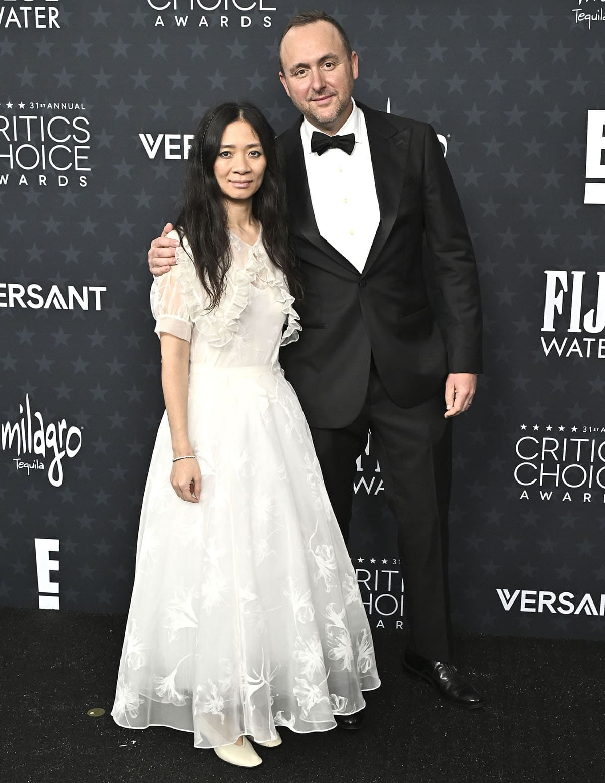Filmmaker Chloé Zhao, with film producer Nicolas Gonda, looks ready to walk down the aisle in a white sheer lace Rodarte dress with a ruffled capelet