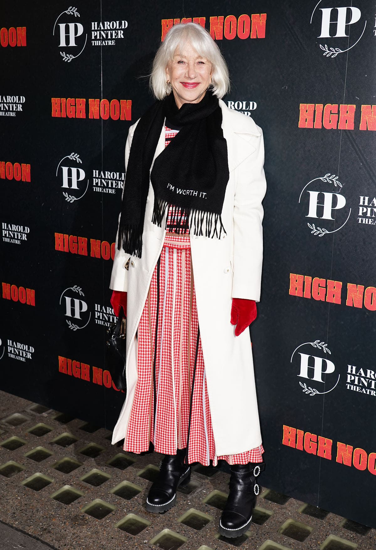 Dame Helen Mirren attends the High Noon West End opening night at the Harold Pinter Theatre on January 9, 2026, grounding her red houndstooth maxi dress and white coat with chunky black biker boots featuring pearl-trimmed soles and statement buckles