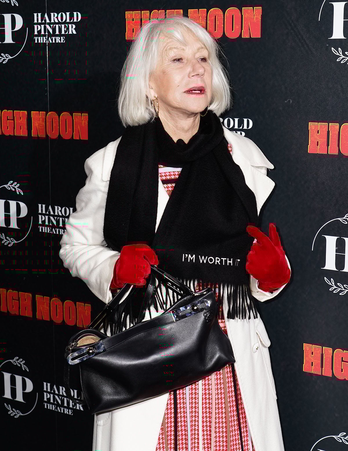 Dame Helen Mirren pairs her boots with a red houndstooth dress, a white cape, red gloves, and a black scarf