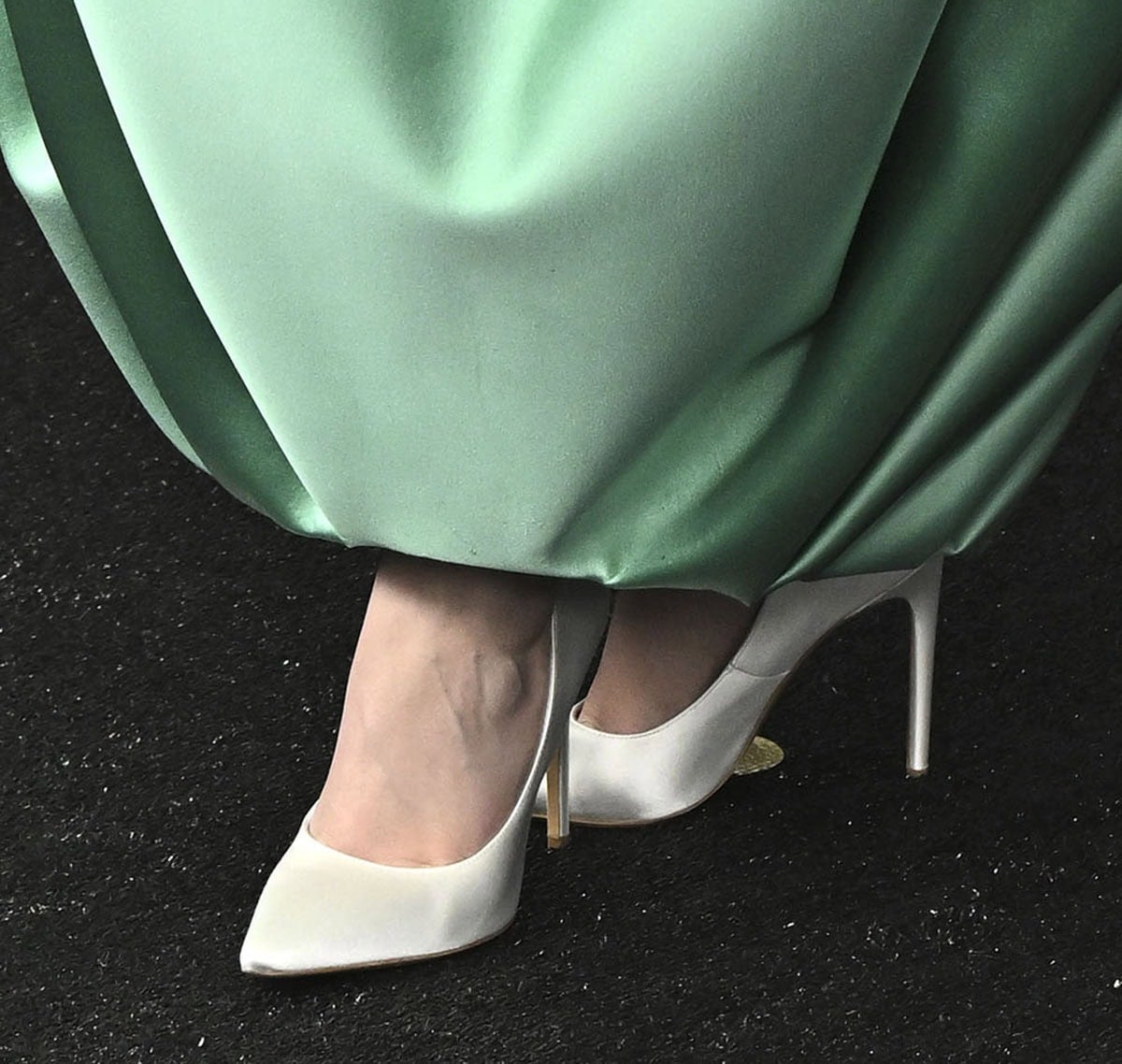 Erin Doherty offsets her sculptural green Louis Vuitton gown with crisp white satin pumps, letting their sharp silhouette balance the dress’s bold architecture