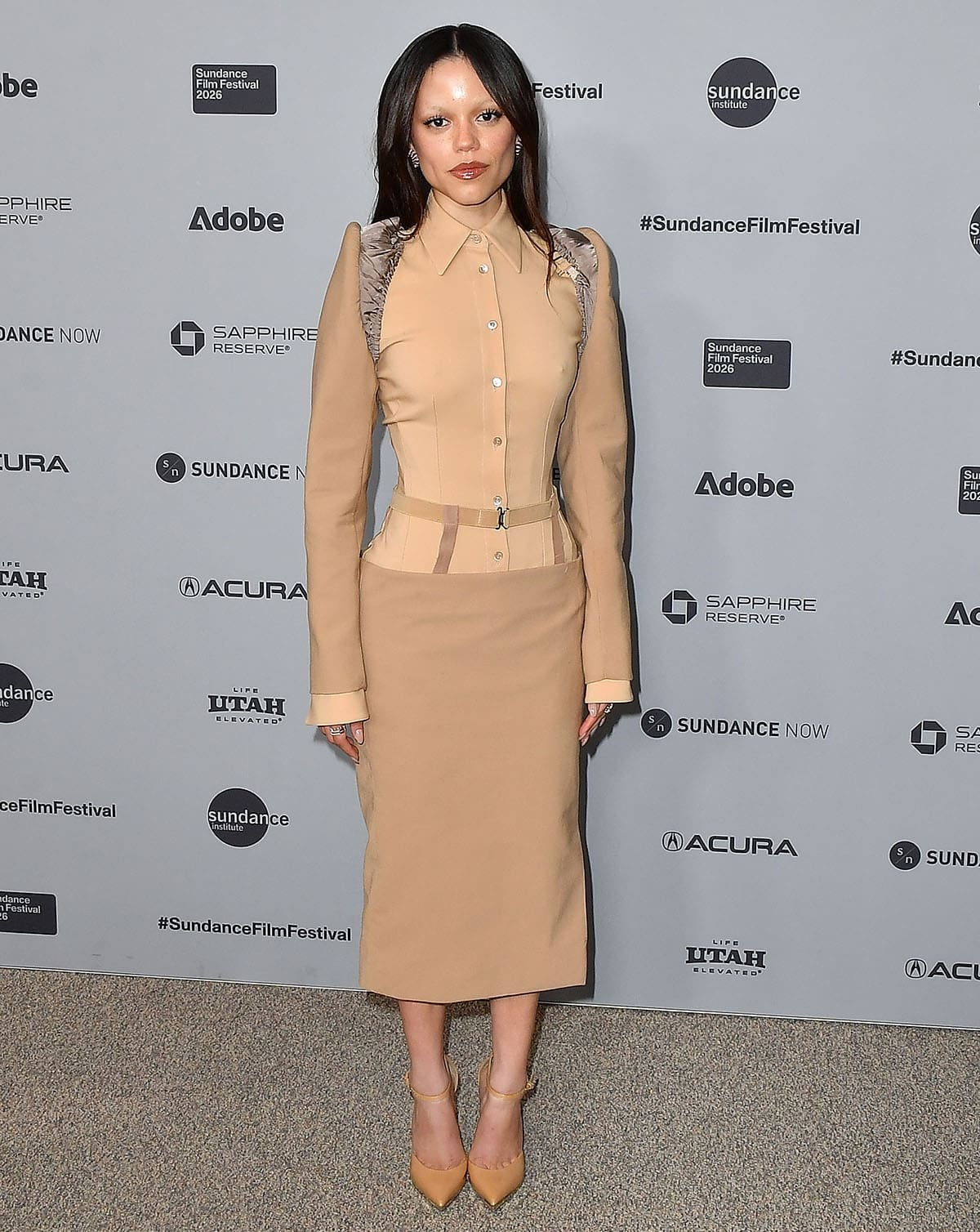 Jenna Ortega looks sharp and modern in a structured beige and camel Mugler shirt with a matching low-rise pencil midi skirt hanging from a suspender-like belt