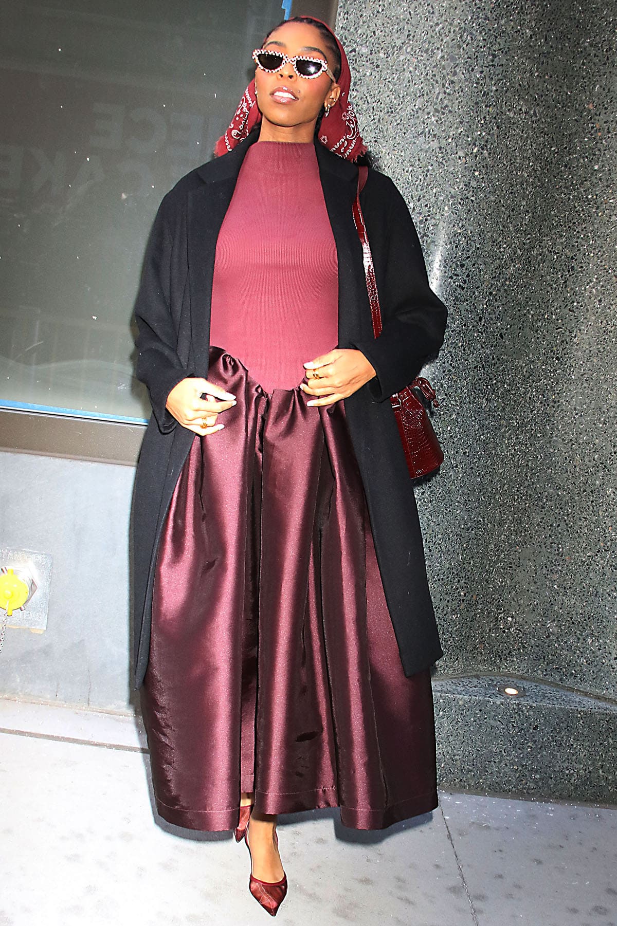 Jessica Williams pairs her burgundy mesh pumps with a burgundy Marques’Almeida dress featuring a ribbed top with a mock neck, cap sleeves, and a basque waist that flows into a voluminous mikado skirt