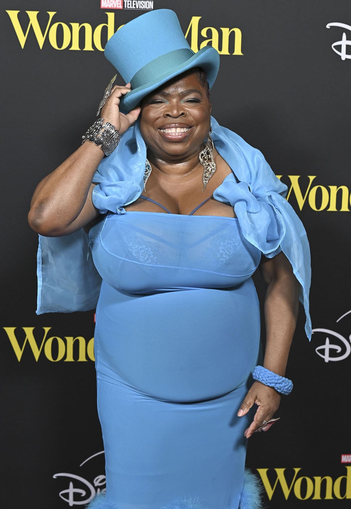 Shola Adewusi wears a blue Addicted to Fits gown with a feathered hem, a matching blue top hat, and a shawl
