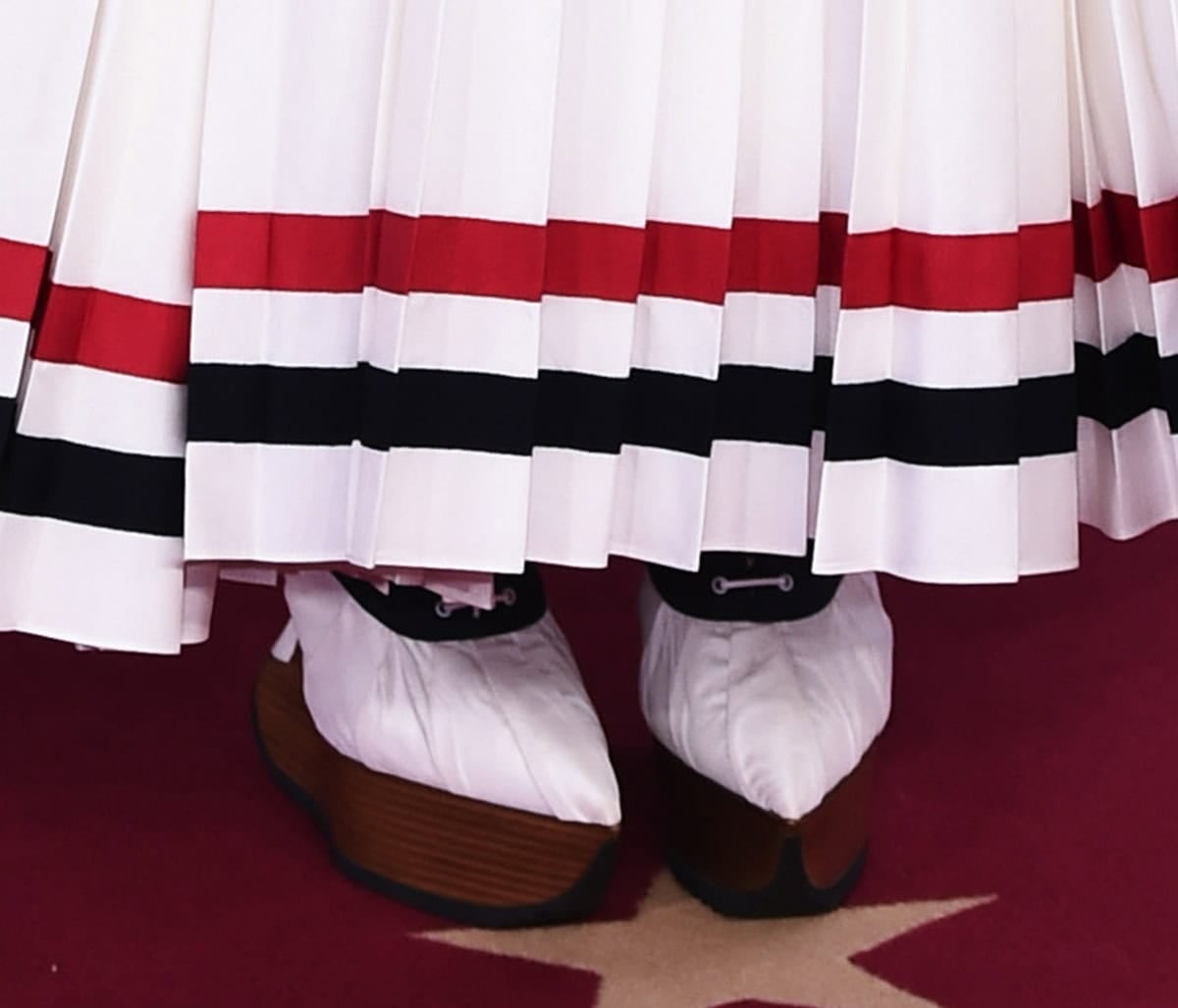 Audrey Nuna wears a pair of quirky shoes from Thom Browne's Spring/Summer 2023 collection, featuring wooden platforms, pointed toes, white fabric uppers with a black panel, and a white lace-up closure