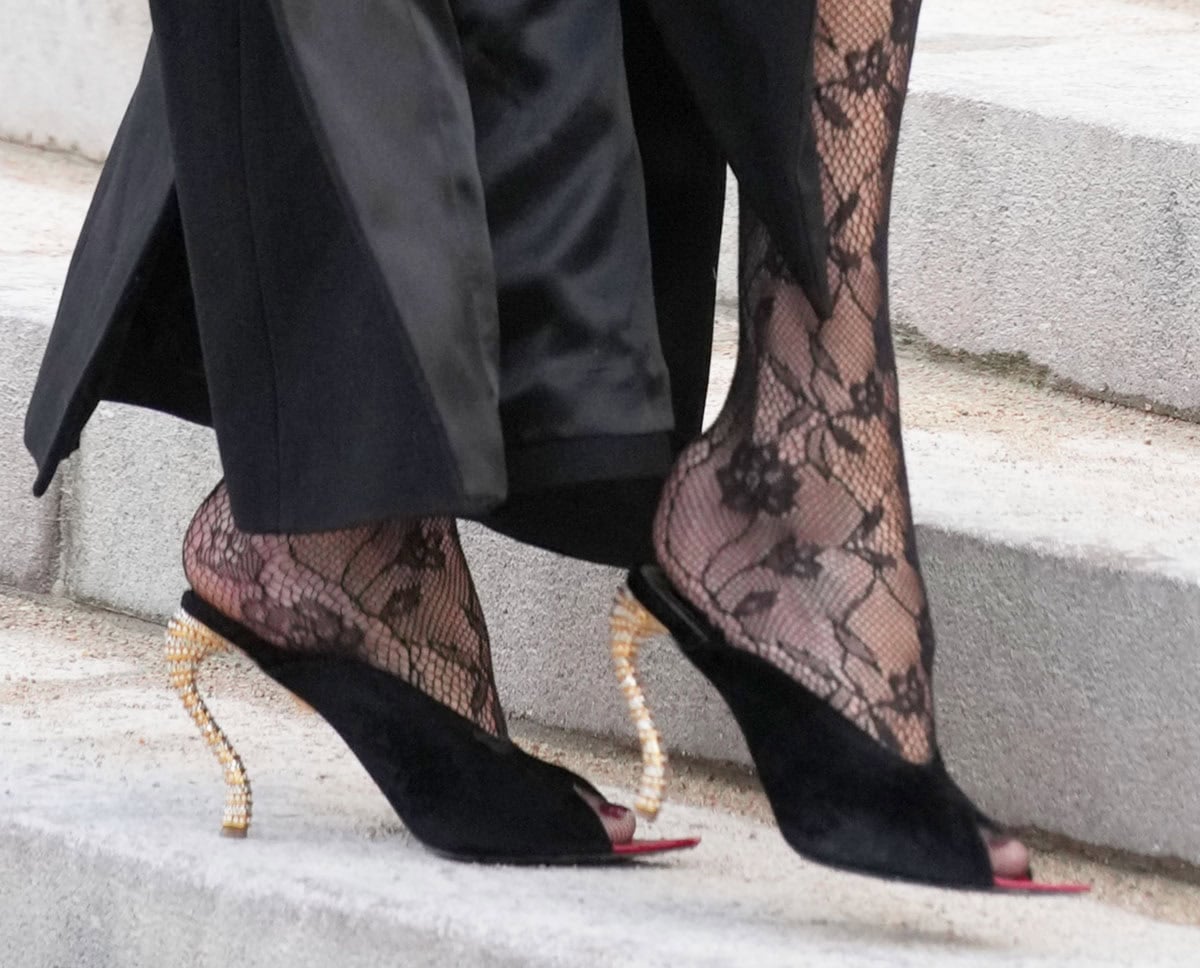 Carla Bruni wears the eye-catching Bijoux mules in black velvet with peep toes and sculptural S-shaped heels finished with pearls and rhinestones