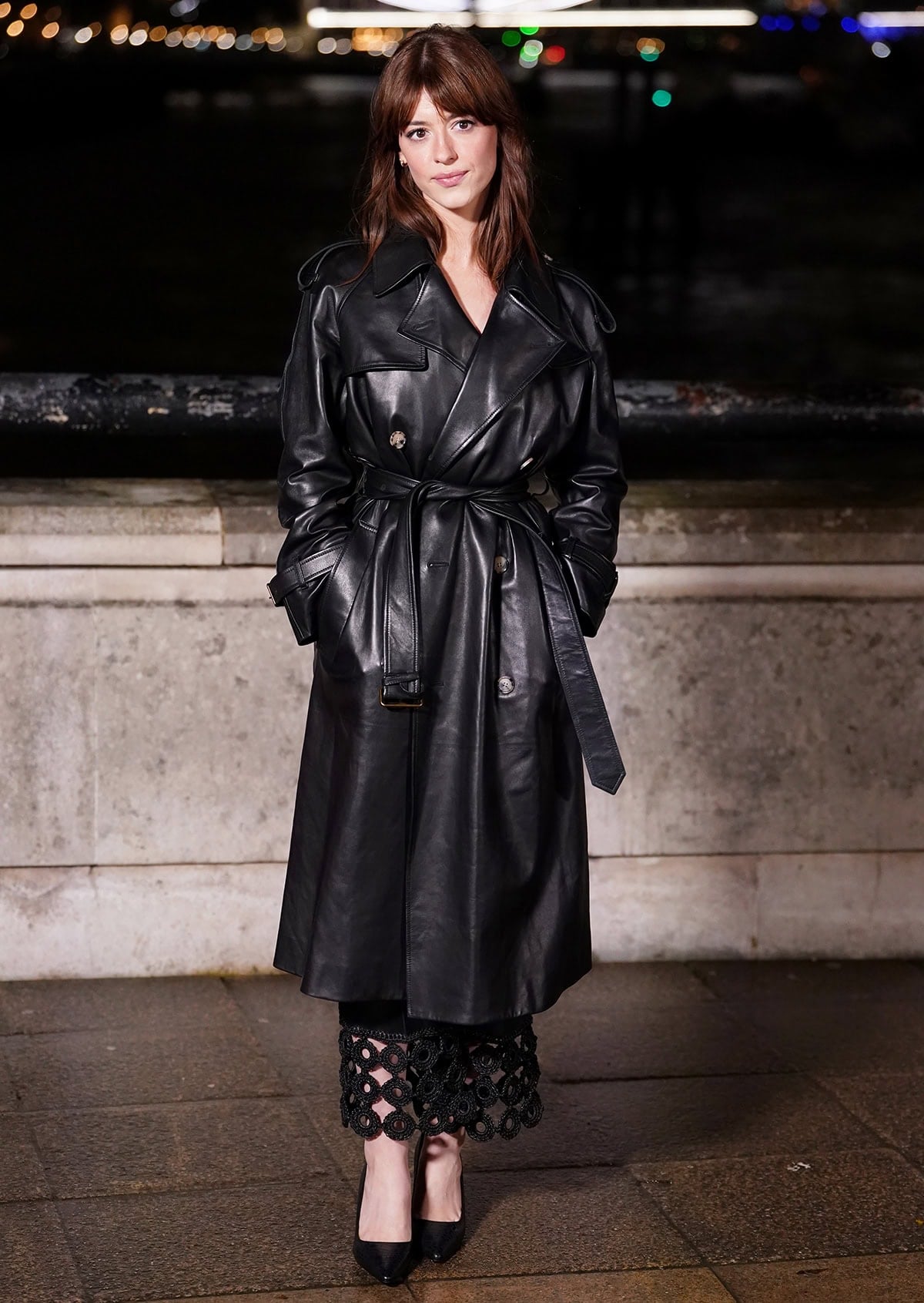 Daisy Edgar-Jones pairs her classic black pumps with a black dress featuring a crochet-adorned hemline and a black leather trench coat