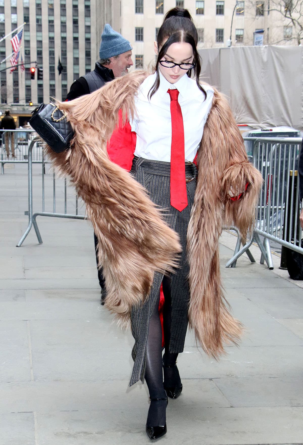 Dove Cameron wears a pinstriped white cotton poplin Ferrari shirt with a red necktie and a gray pinstripe wool pencil midi skirt with a wrap-style front