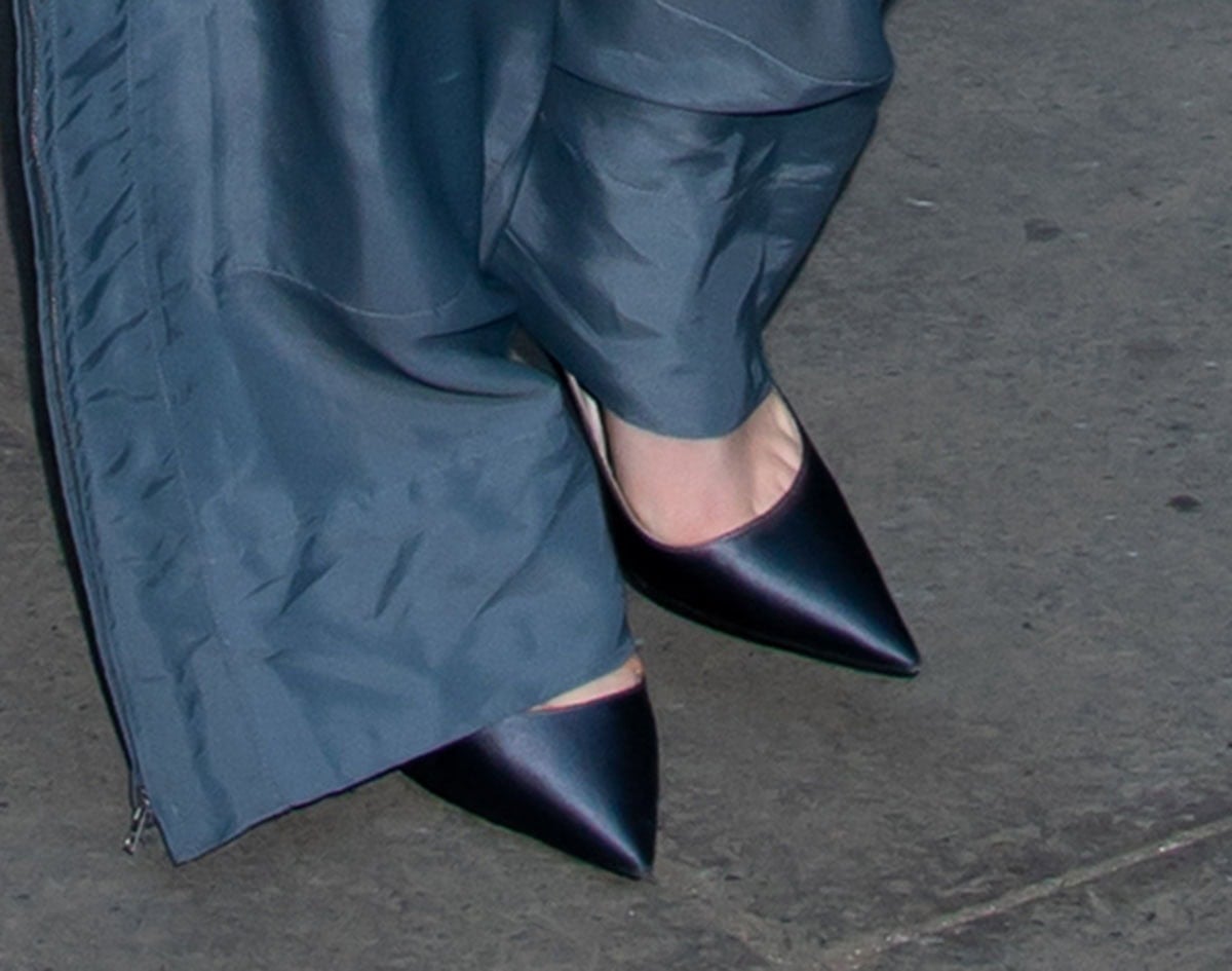 Dove Cameron finishes her modern tailoring with sleek satin pointed-toe pumps, their sharp silhouette and subtle sheen echoing the cool tones of her fluid gray trousers