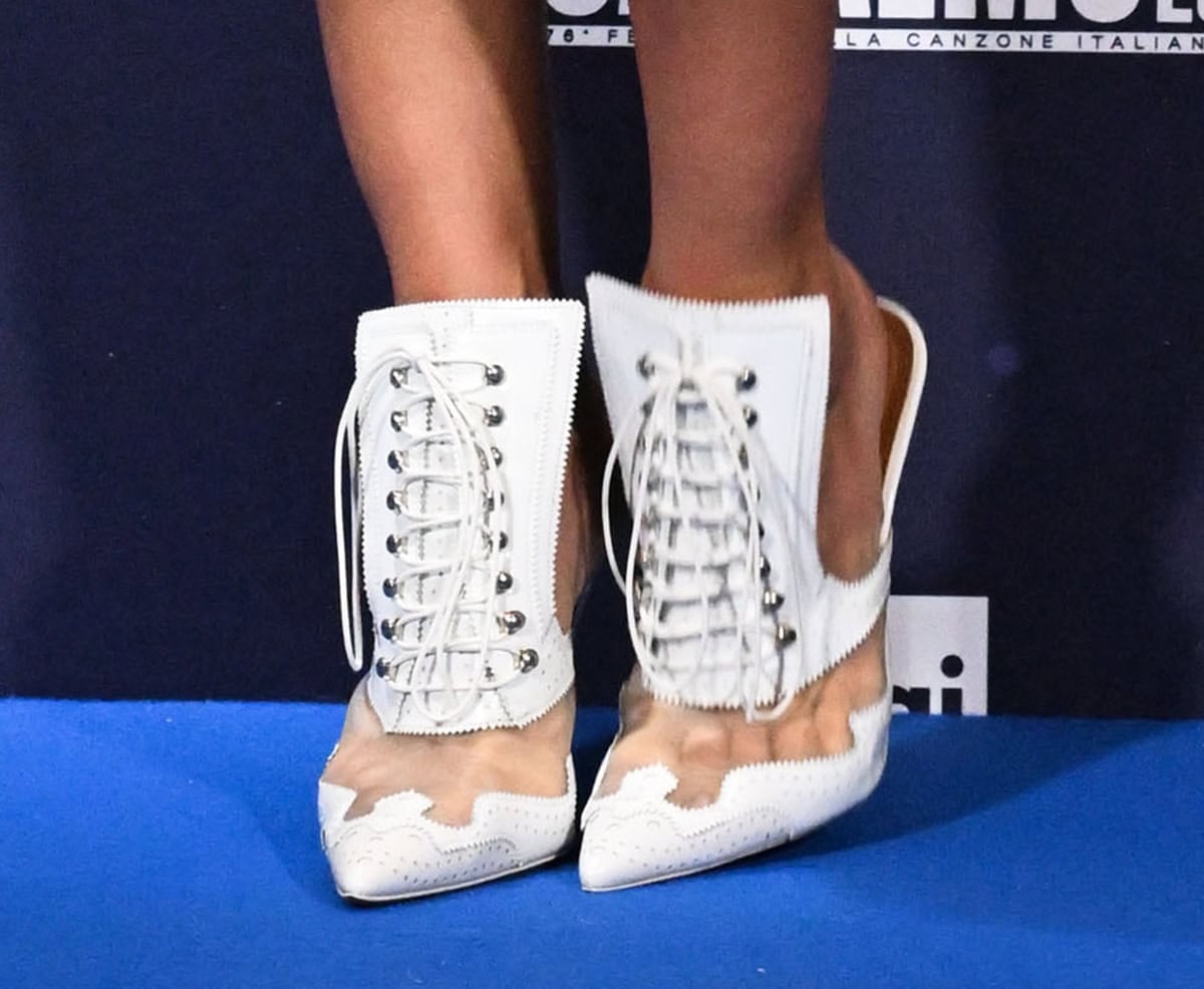 Irina Shayk slips into the white Givenchy “Rooja” mules featuring corset-style lace-up detailing at the front, white lace inserts, an open back, and slim high heels
