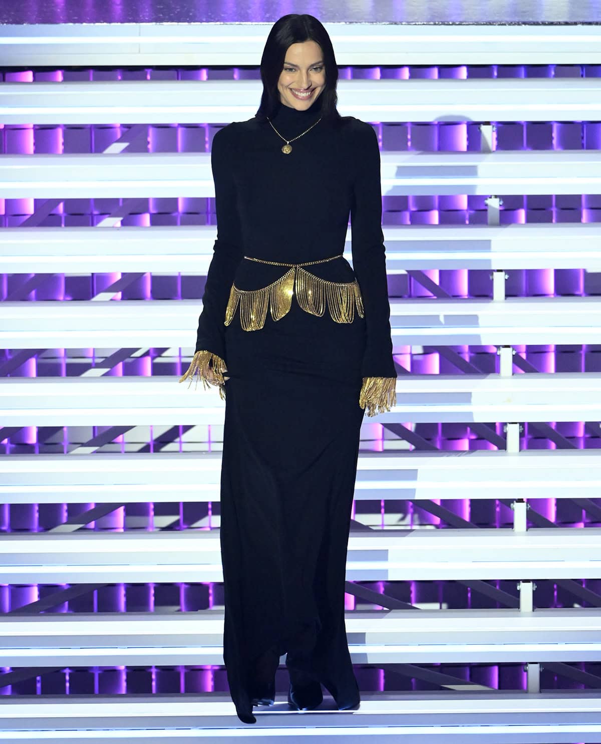 Irina Shayk goes the modest route, pairing her pumps with a turtleneck dress with gold chain fringe accents at the waist and cuffs