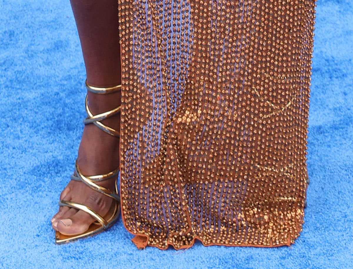 Issa Rae wears the strappy metallic gold Le Silla “Bella” sandals featuring crisscrossing straps and pin-thin stiletto heels