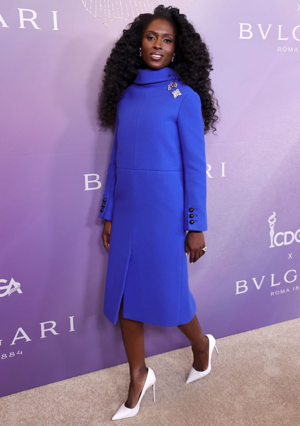 Jodie Turner-Smith stuns in a boxy, mod-style cobalt blue Marc Jacobs midi dress featuring a high neck, long sleeves, and silver and black brooches