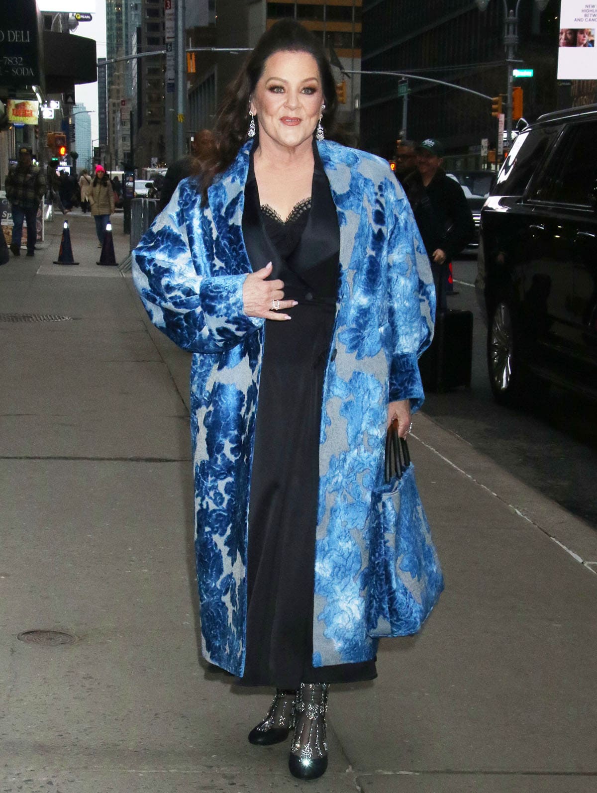 Melissa McCarthy visits The Late Show with Stephen Colbert in a blue floral jacquard coat, a black satin dress, and crystal mesh ankle boots